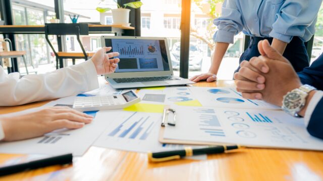 A group of business people are looking at various graphs around a wooden table for an internal audit.