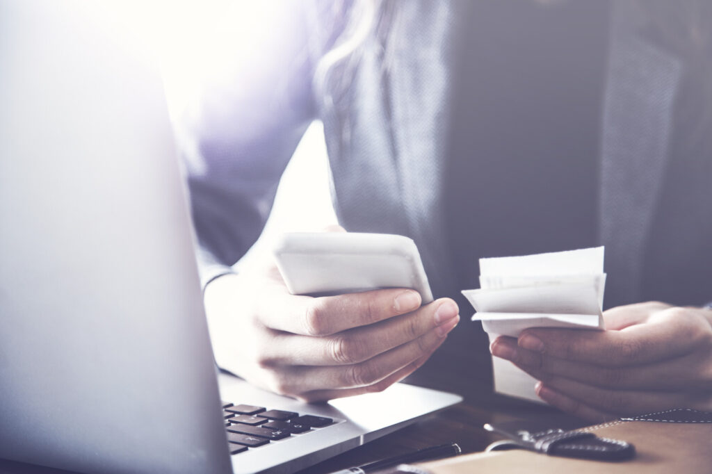 Person checking receipts against a phone and laptop