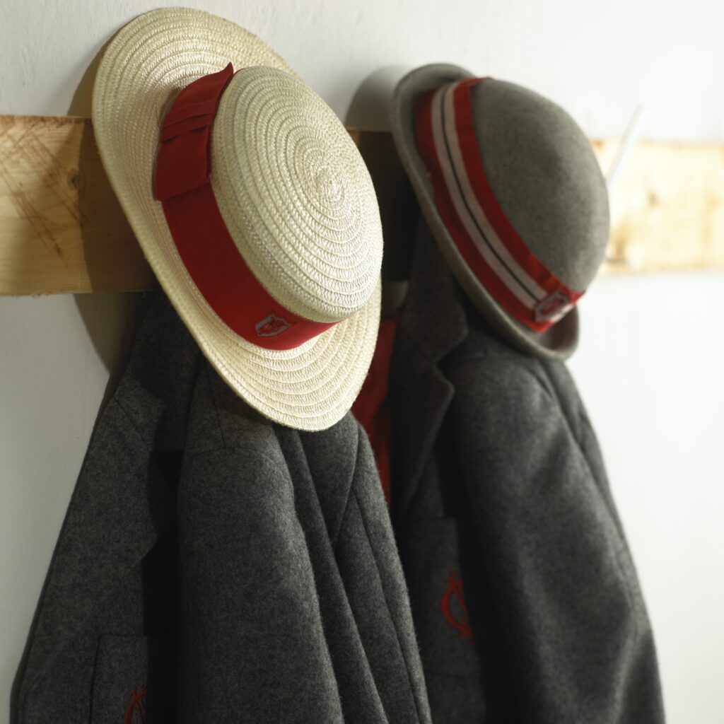 Private school hats and blazers hanging on wooden hooks|
