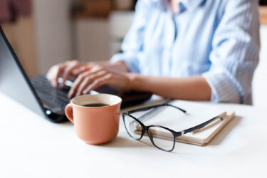 Close up of female business owner completing finances on a laptop, with a mug of coffee and glasses next to her.