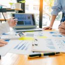 A group of business people are looking at various graphs around a wooden table for an internal audit.