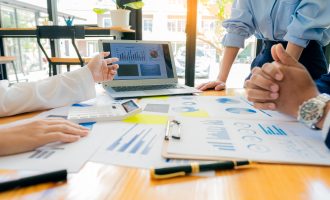 A group of business people are looking at various graphs around a wooden table for an internal audit.