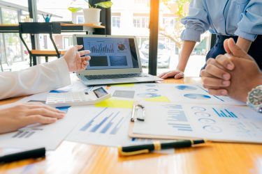 A group of business people are looking at various graphs around a wooden table for an internal audit.