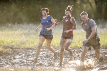 Charity runners run through a muddy puddle in a field